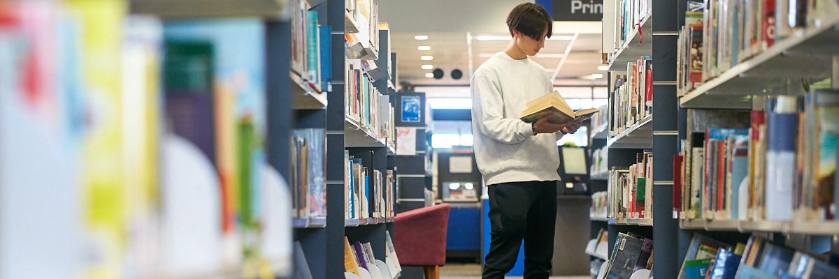 Borrower reading library book in front of shelf