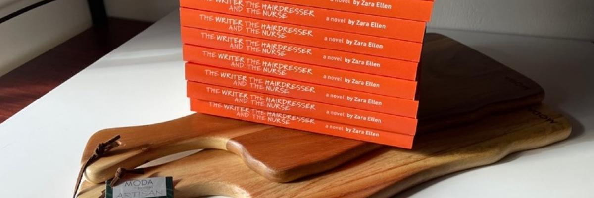 A stack of book copies, all orange with white text, stacked neatly on top of a wooden board.