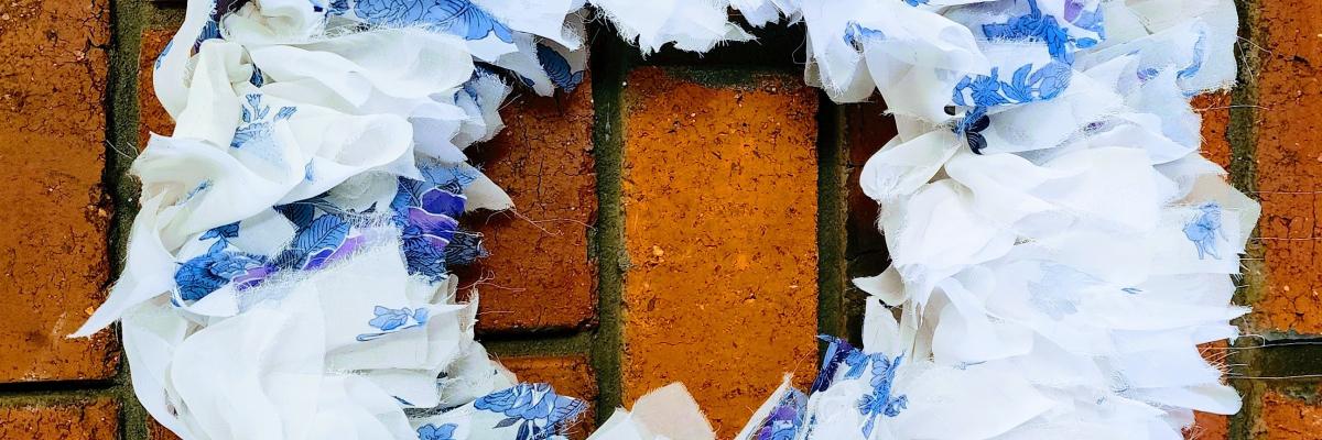 A brick wall with a Christmas wreath in front of it, made of blue and white fabric scraps