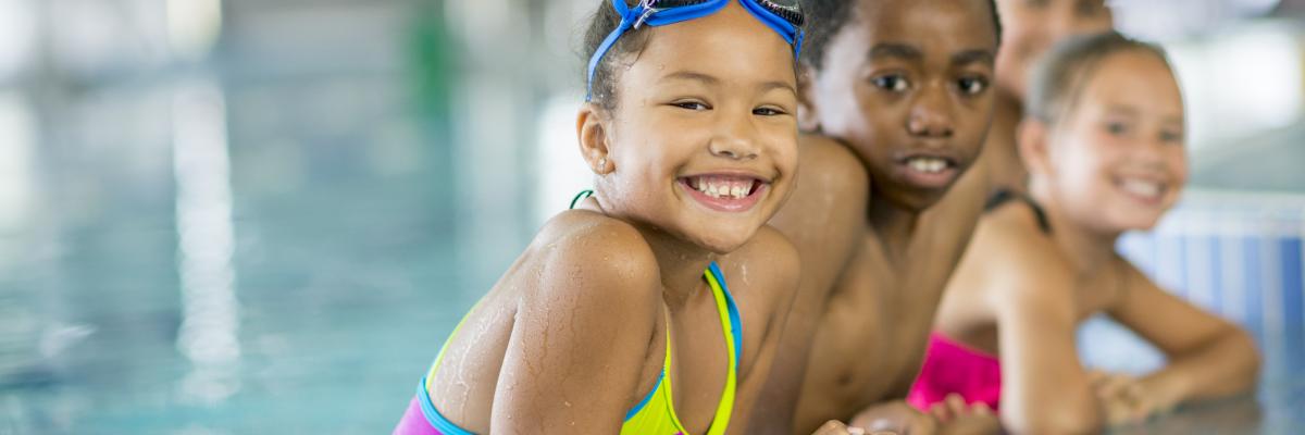 Children in a pool leaning against the ledge smiling