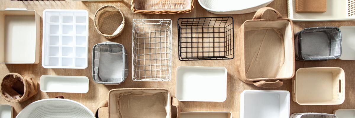 A large selection of different organisational containers, some rectangular, some oval, some wiry and some fabric, arranged on a beige background.