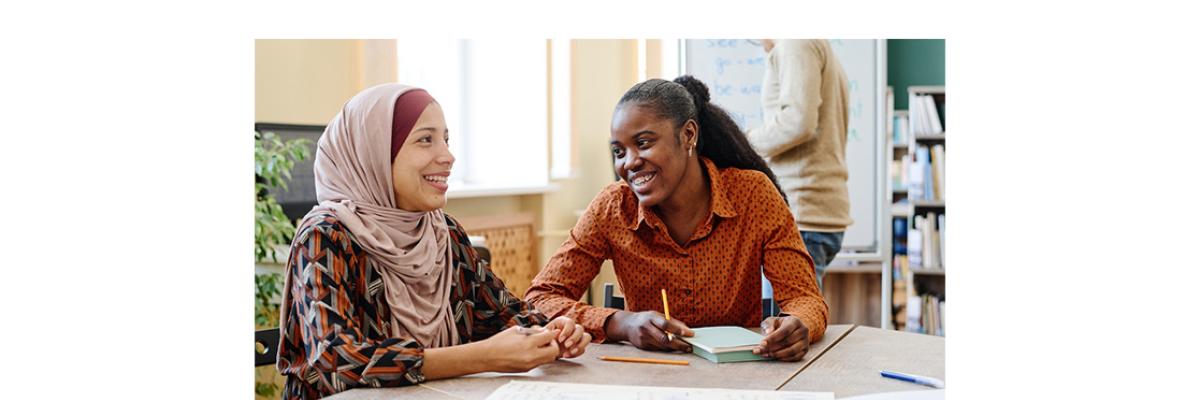 Two multicultural women sitting at a desk with pens and paper