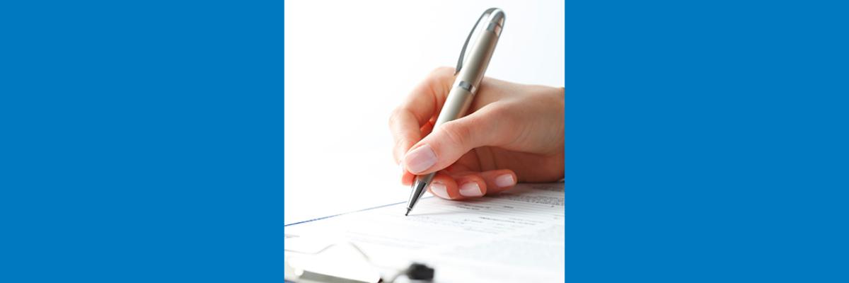 Hand holding a pen filling in a form on a clipboard