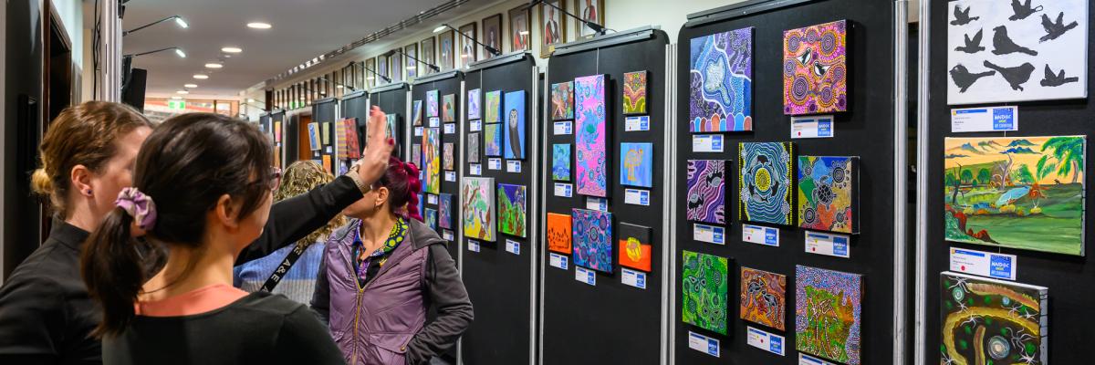 Exhibition with Aboriginal artwork and on the left people are observing it
