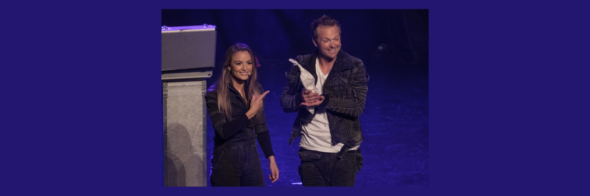 Adam and Selina - The Magicians. On stage. Adam is holding a dove, and Selina is smiling and pointing at it.