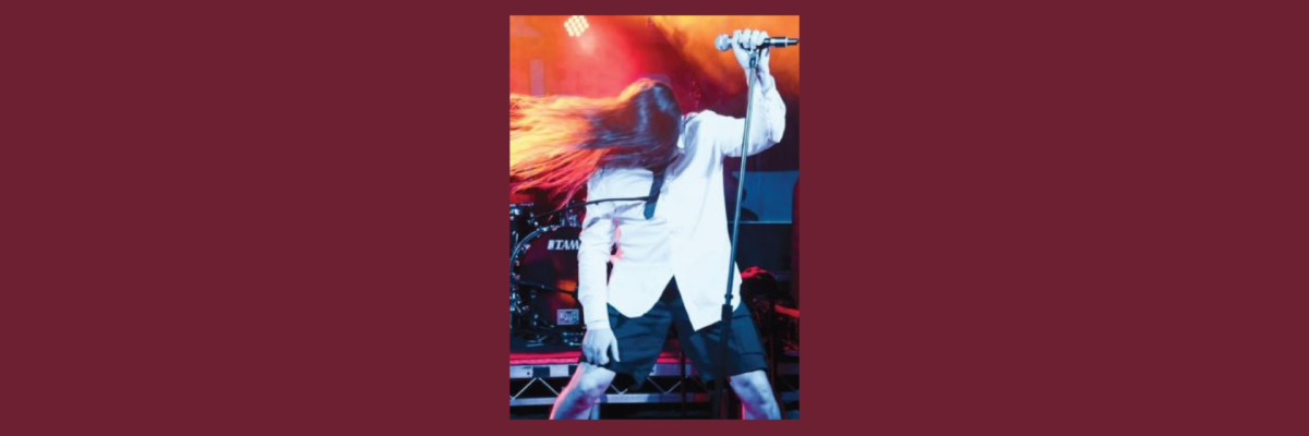 Rock singer with long hair swings it around onstage, whilst holding a microphone on a stand.