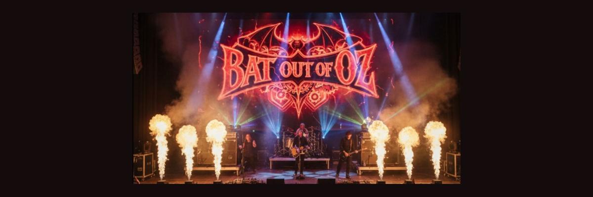 Rock band playing on a stage with neon sign reading "Bat out of Oz" behind them. Pyrotechnics on the sides of the stage.