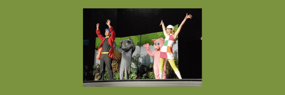 Goldilocks, 2 bears and a man stand on stage, with their arms raised in the air looking joyful.
