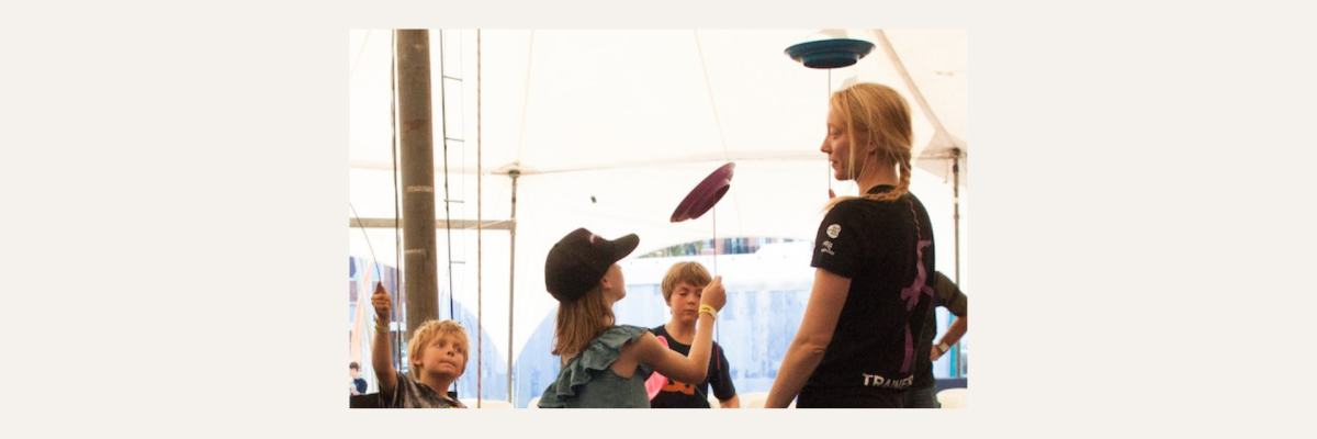Children spinning plates, with a circus instructor supervising them