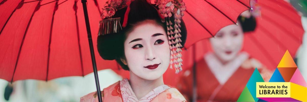 Two geisha in traditional white makeup, dressed in red and pink kimonos, under red parasols