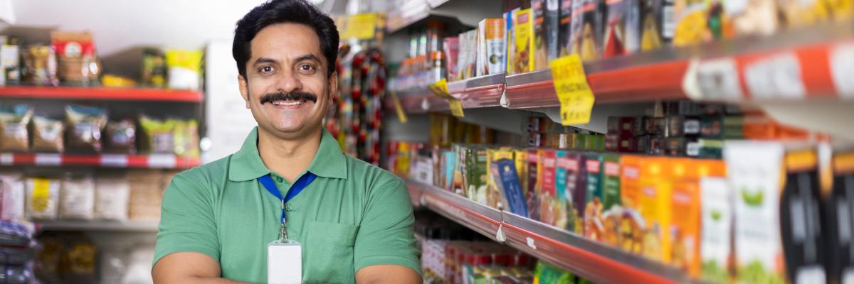 A proud business owner stands beside shelves of stock.