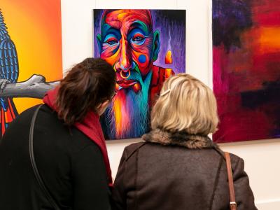 Two women viewing a bright and vivid artwork at the Community Art Exhibition and Awards 2021