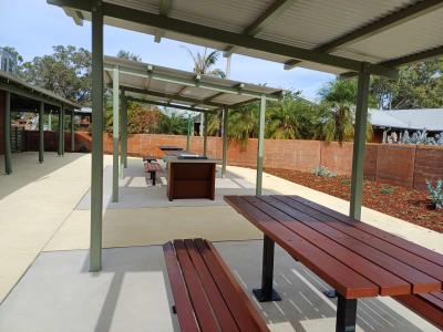 Courtyard showing three picnic seats under shelter with barbecue inbetween