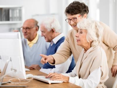 A group of seniors sitting at a desk, pointing or looking at a computer screen