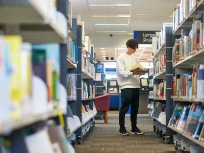 Borrower reading library book in front of shelf