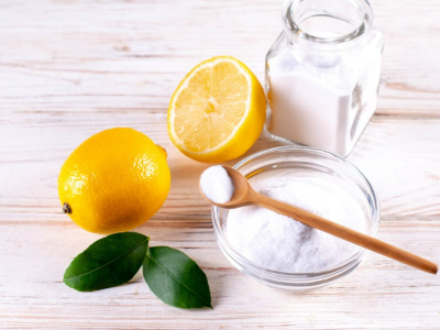 Natural cleaning ingredients, including leaves, lemons, a glass jar of baking soda, a glass bowl of baking soda, and a wooden spoon.