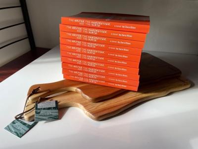 A stack of book copies, all orange with white text, stacked neatly on top of a wooden board.