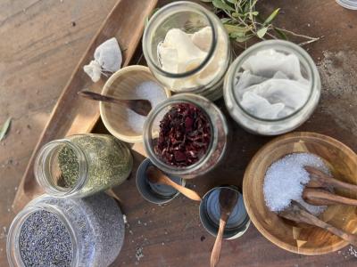 A variety of glass jaws and wooden bowls containing organic ingredients like lavendar, rose petals, salt etc.