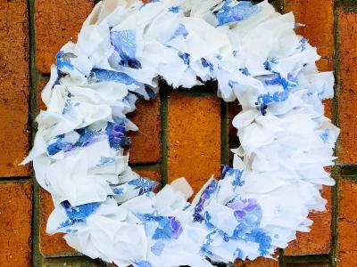 A brick wall with a Christmas wreath in front of it, made of blue and white fabric scraps