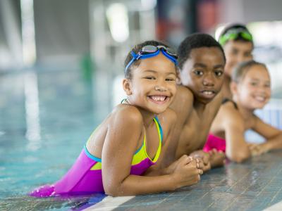 Children in a pool leaning against the ledge smiling