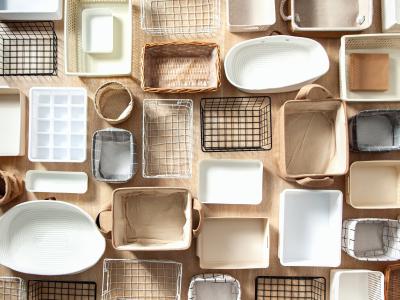 A large selection of different organisational containers, some rectangular, some oval, some wiry and some fabric, arranged on a beige background.