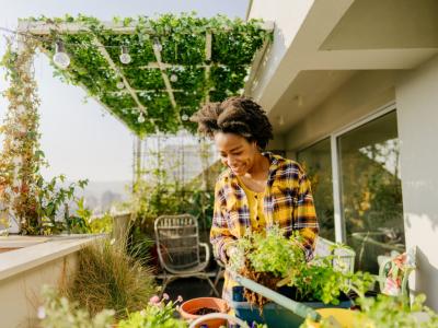 A dark-skinned woman on a rooftop balcony, tending to her many growing plants