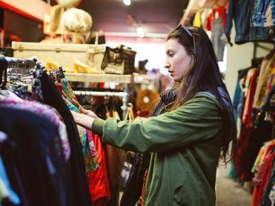 A woman in a green jacket, sorting through clothes on a rack in an op shop or thrift store