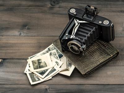 An antique camera lying on a dark brown table, next to a collection of black and white photos