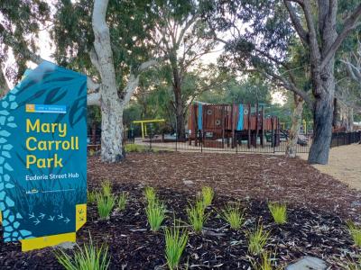 Mary Carroll Park entrance sign with playground in background surrounded by trees