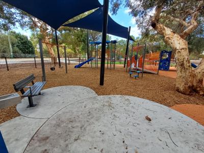 Boyle Playground bench seat with play structure and shade sails in background
