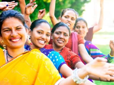 A line of smiling Indian women in colourful saris, raising their hands in dance