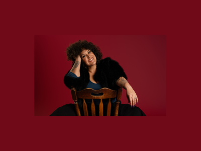 Casey Donovan sitting on a chair, in front of a red background.