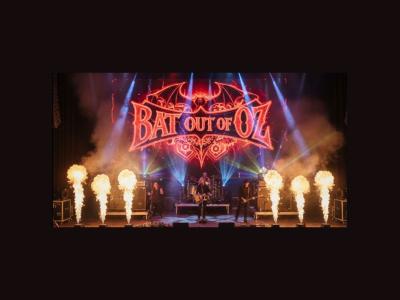 Rock band playing on a stage with neon sign reading "Bat out of Oz" behind them. Pyrotechnics on the sides of the stage.