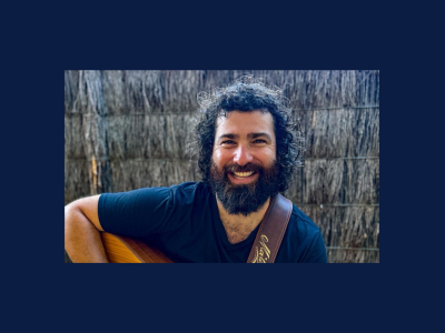 Jeff sits smiling at the camera, with an acoustic guitar on his lap