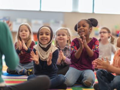 Diverse group of children sitting in front of a teacher clapping their hands