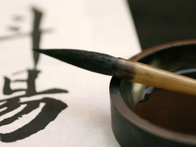 Chinese calligraphy in black ink on white paper, with a calligraphy brush resting nearby