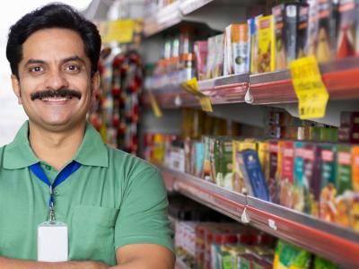 A proud business owner stands beside shelves of stock.